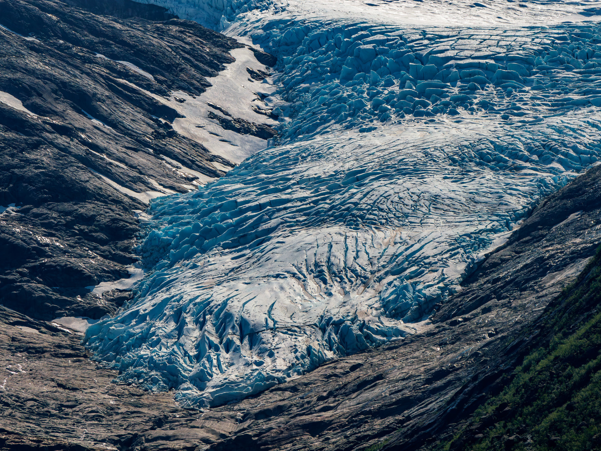 Blue glacier ice flowing between dark rocky ridges