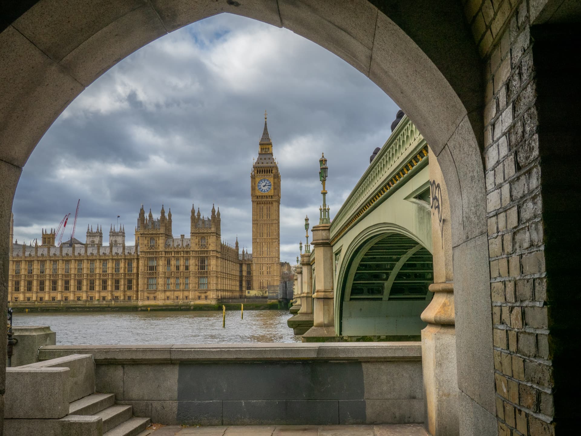 Big Ben and the Houses of Parliament framed by a stone arch beside Westminster Bridge, London