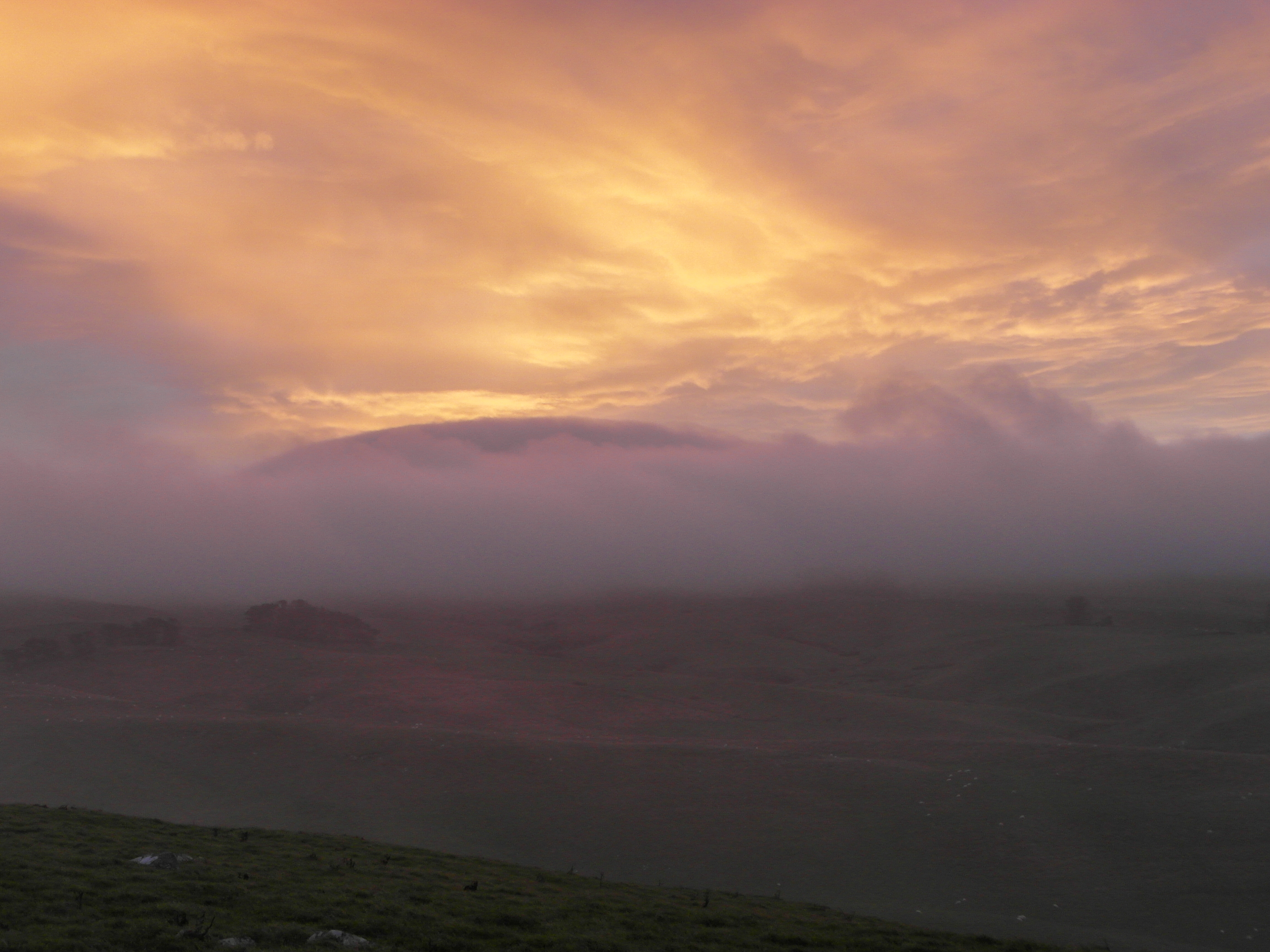 Golden orange sky above dark hills and layers of purple-toned mist.