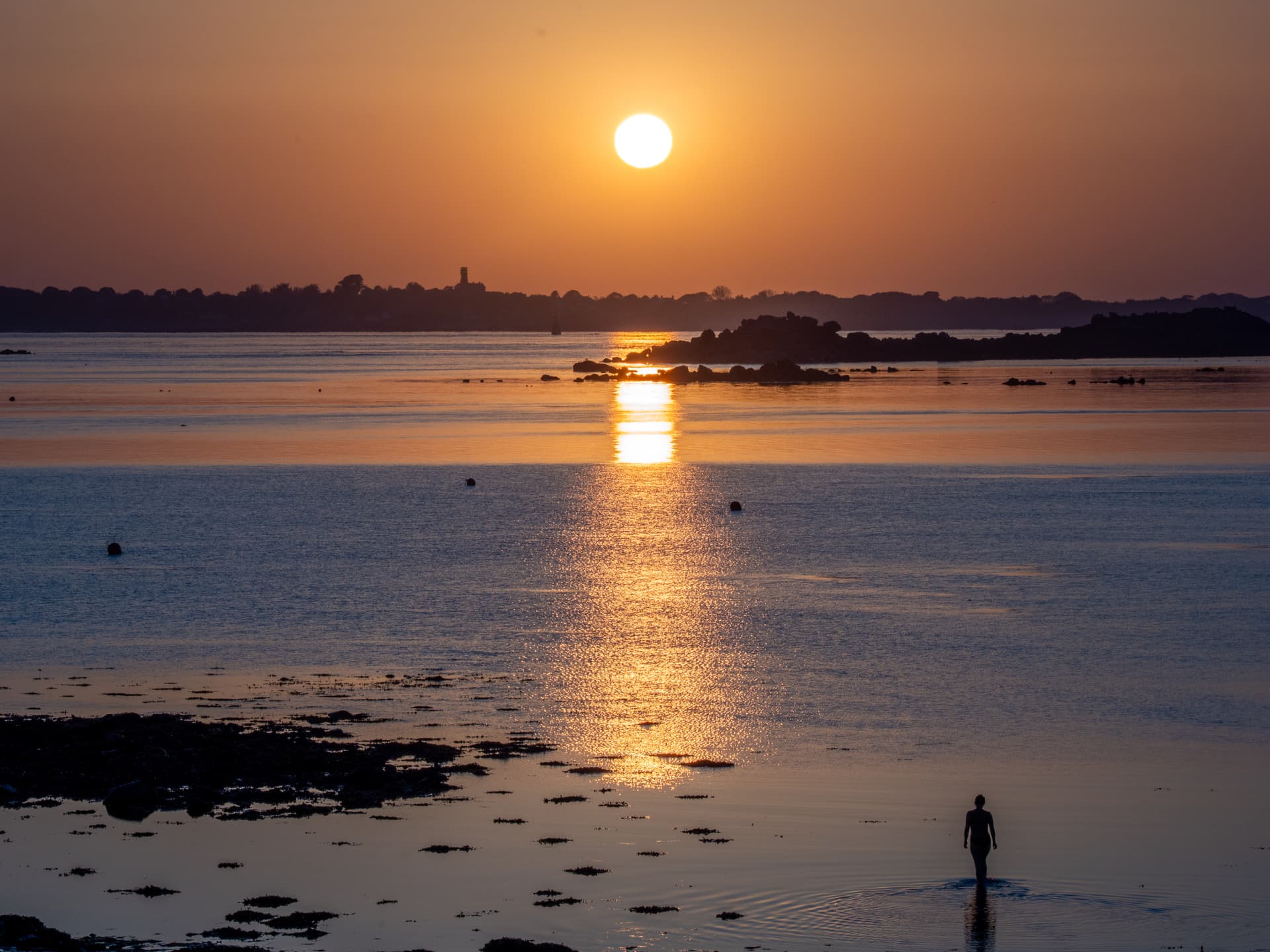 Swimmer wading into a calm sea beneath an orange sunset